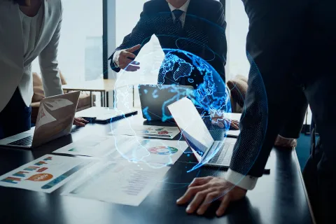 Business team in a meeting with laptops and charts, discussing a digital 3D globe hologram projection above the table.