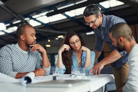 Team of four diverse professionals collaborating over documents in a modern office setting.