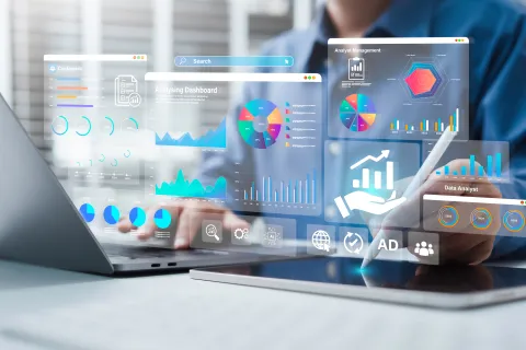 Person working on laptop and tablet with digital data analytics dashboards and charts on screen.
