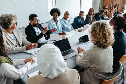 Diverse team of professionals having a discussion around a conference table with laptops in a bright office.