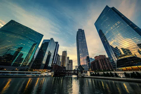 Chicago skyline at sunset with reflective glass skyscrapers along the Chicago River and calm water in foreground