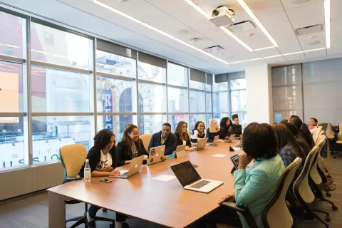 Diverse group of professionals collaborating around a large conference table with laptops in a modern office.