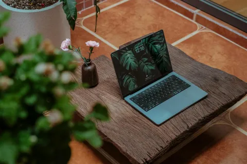 Modern laptop with green leaf wallpaper on wooden table next to flower vase and plant indoors