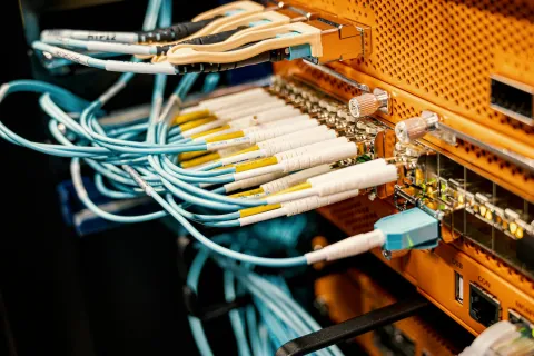Close-up of fiber optic cables connected to an orange network switch in a server room setup.