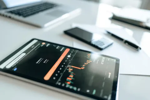 Tablet displaying financial chart with bar graphs on desk alongside laptop, smartphone, and pen.