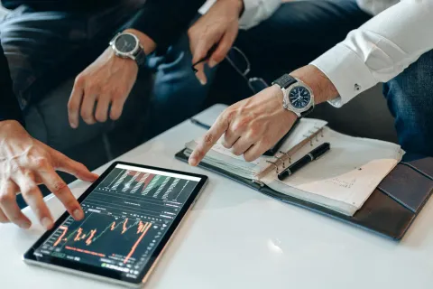 Two professionals analyzing financial data on a tablet with charts and notes on a table during a meeting