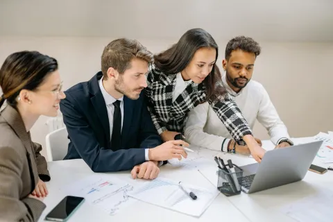 Team of diverse professionals collaborating over documents and laptop in modern office meeting room.