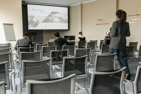 Business professionals wearing masks attend a socially distanced presentation on business analysis in a conference room.