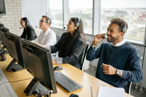 Customer service team wearing headsets and working on computers in a modern office with large windows.