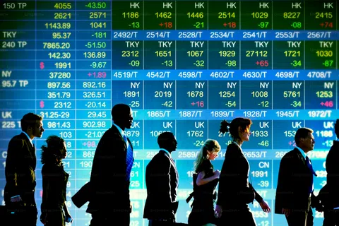 Silhouettes of business people walking in front of a large digital stock market ticker displaying financial data.