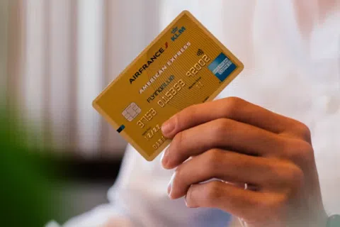 Hand holding a gold Air France KLM American Express credit card with chip and contactless payment icons.