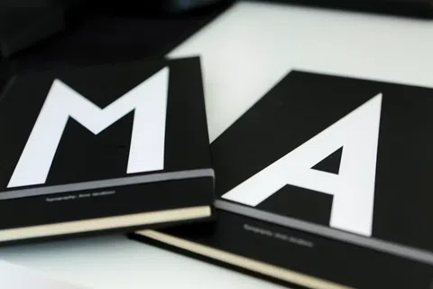 Two black notebooks with large white letters M and A on the covers placed on a white surface.