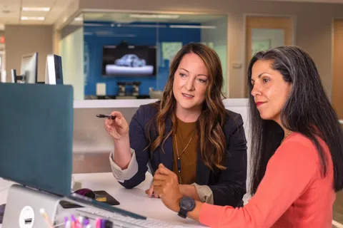 Two professional women discussing and pointing at a computer screen in a modern office setting.