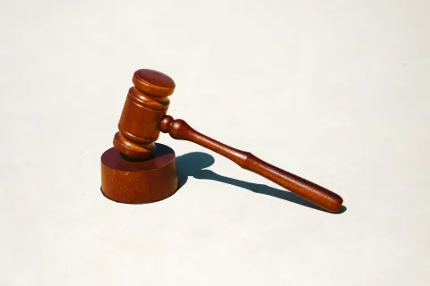 Wooden judge's gavel and sound block casting shadow on a light surface representing law and justice.