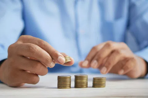 Person stacking coins in three neat piles on a white table, focusing on saving and counting money.