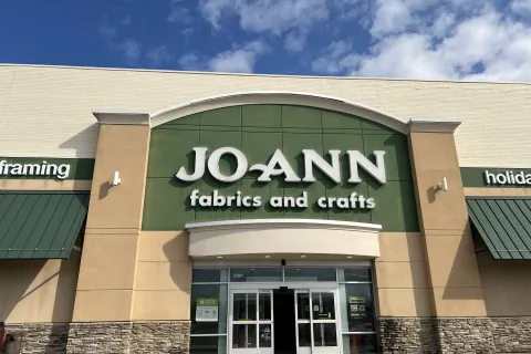 Front entrance of JOANN fabrics and crafts store with green and beige exterior under a blue sky