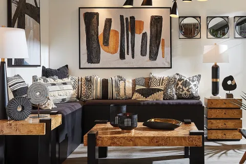 Modern living room with black sectional sofa, patterned pillows, wooden tables, abstract art, and contemporary lighting.