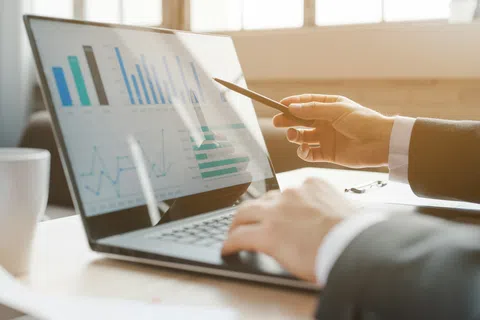 Business professional pointing at financial charts on laptop screen during office meeting