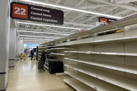 Empty grocery store shelves in aisle 22 for canned soup, beans, and vegetables with few shoppers.