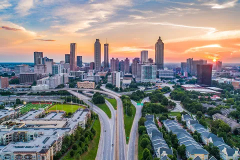 Sunset over Atlanta skyline with highways, residential areas, and green spaces in the foreground.