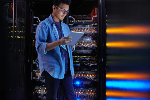 IT technician checking server rack with tablet in data center room with colorful LED lights.