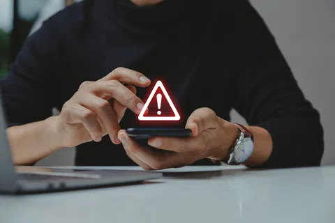 Person holding smartphone with red warning alert icon showing potential mobile security threat.