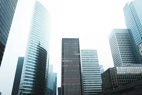 Modern glass and steel skyscrapers forming a city skyline under an overcast sky.