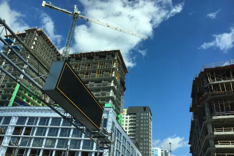 High-rise buildings under construction with a crane against a blue sky with clouds