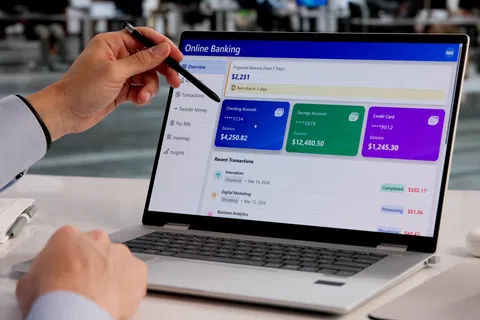 Person using a laptop displaying an online banking dashboard with account balances and recent transactions.