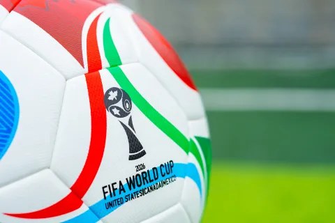 Close-up of the 2026 FIFA World Cup official soccer ball with colorful red, green, and blue stripes on a green field.
