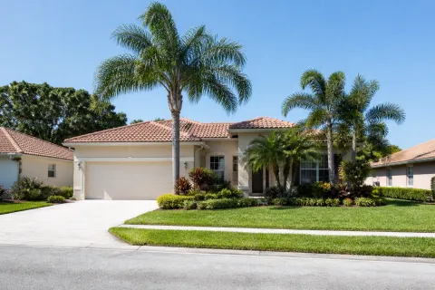 Single-story house with tiled roof, palm trees, and green lawn under a clear blue sky.