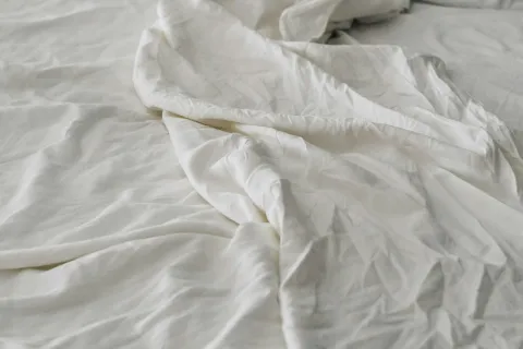 Unmade bed with white rumpled sheets and a matching pillow creating a cozy, lived-in atmosphere.