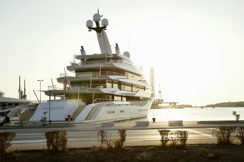 Luxury white yacht docked at harbor with calm water and golden sunset in the background.
