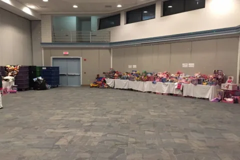 Large room with tables lined with toys and a child standing on the left side looking at a phone.