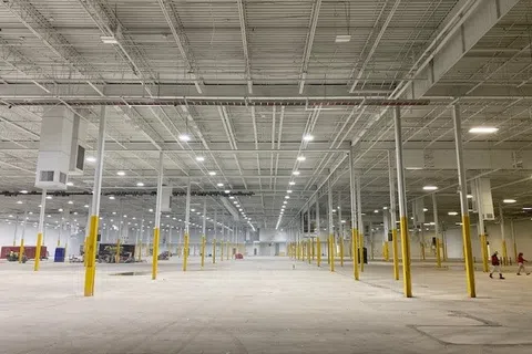 Vast empty warehouse interior with yellow safety poles and bright overhead lighting.
