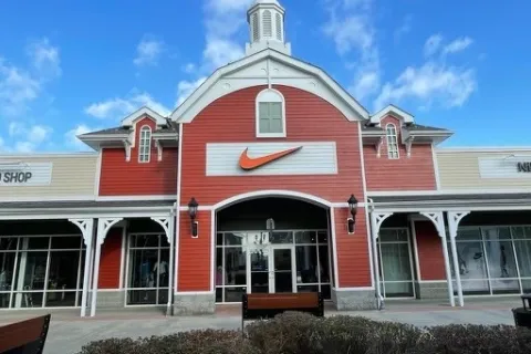 Exterior of a red and beige Nike store with a large orange swoosh logo under a blue sky