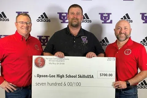 Three men holding a $700 donation check to Upson-Lee High School SkillsUSA in front of a branded backdrop.