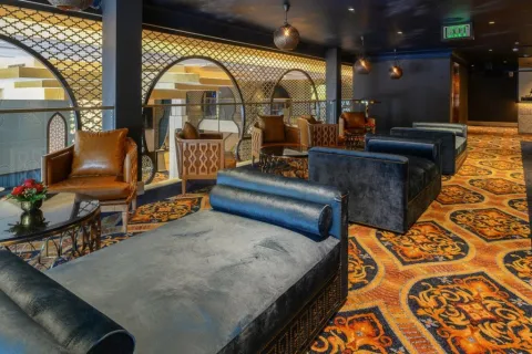 Luxurious lounge area with velvet chaise lounges, leather chairs, and ornate patterned carpet in warm tones.