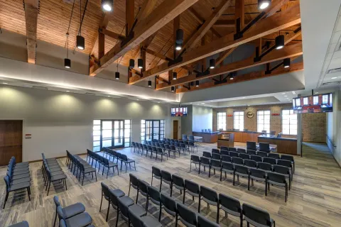 Spacious modern courtroom with wooden ceiling beams, rows of black chairs, and multiple display screens.