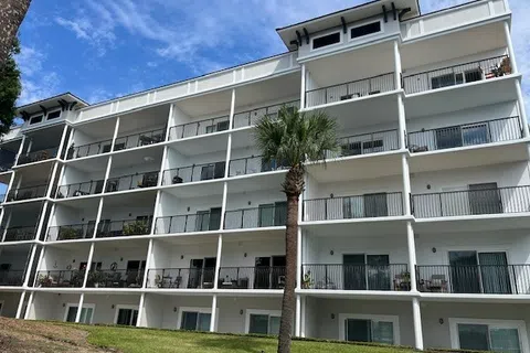 Modern white apartment building with balconies and a palm tree under a blue sky with clouds. Fall Maintenance Checklist for Facility Managers.