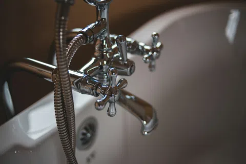 Close-up of vintage chrome bathtub faucet and flexible shower hose on white porcelain tub.