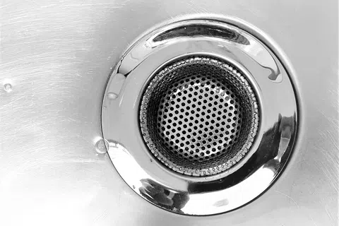 Close-up of a shiny metal sink drain with perforated strainer and brushed steel surface