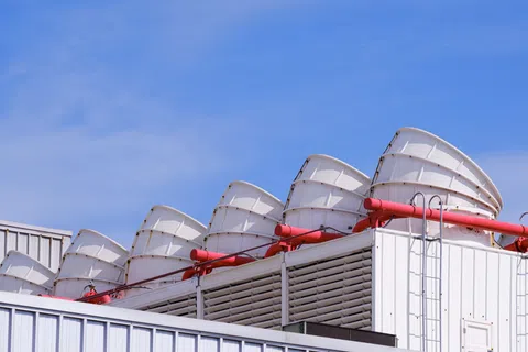 Row of large white industrial ventilation fans with red pipes on a rooftop against a blue sky.