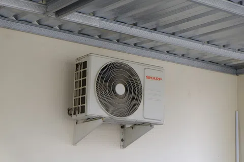 White Sharp brand air conditioning outdoor unit mounted on a wall under a metal roof.