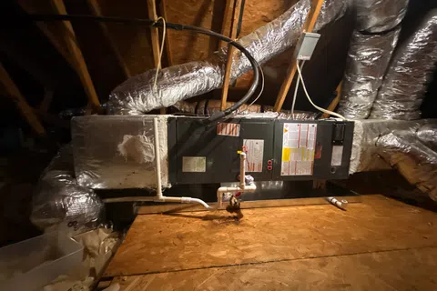 HVAC system with insulated ductwork and pipes installed in a wooden attic space under roof beams.