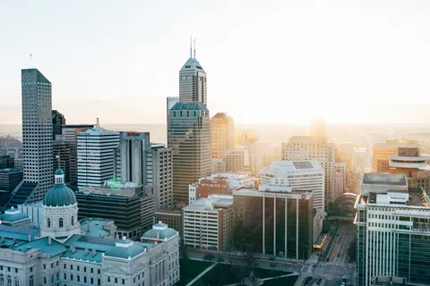 Sunlit skyline of a modern city with tall skyscrapers and historic buildings at sunrise.