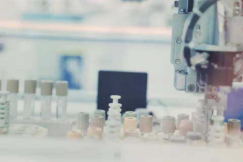Automated laboratory equipment handling multiple test tubes and vials in a clinical setting.