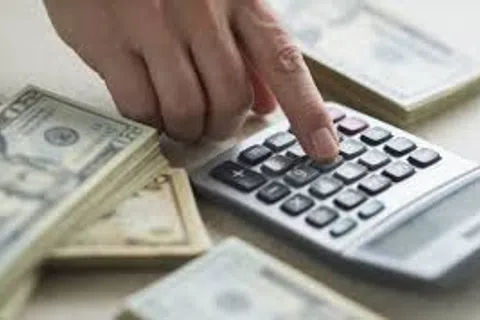 Hand pressing calculator buttons with stacks of US dollar bills on the table for financial calculations.