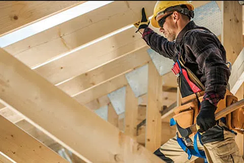 Construction worker with helmet and tools working on wooden roof framing in bright daylight