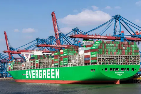 Large green Evergreen container ship loaded with colorful cargo containers docked at Terminal Burchardkai under blue sky.